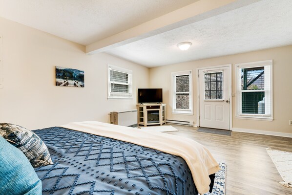 A bedroom with a bed, a TV, and a door leading to a balcony.