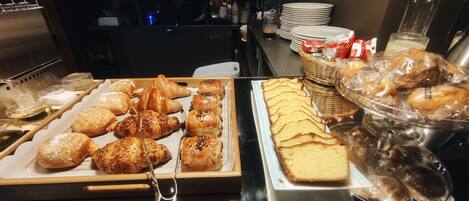 A buffet with various pastries, bread, and a large loaf of bread.