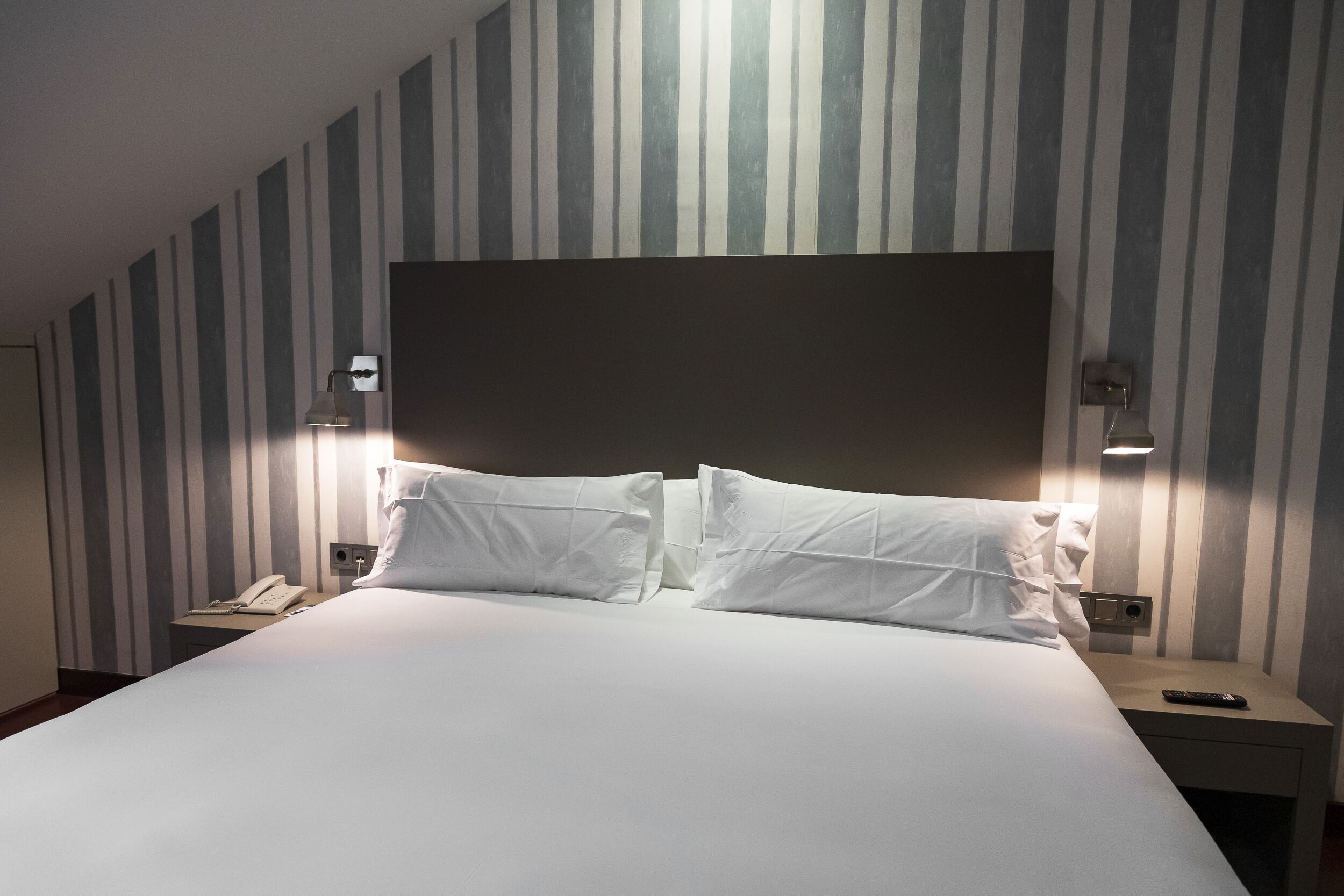 Ein Hotelzimmer mit einem großen Bett, zwei Nachttischen, einem Telefon und einer Fernbedienung.