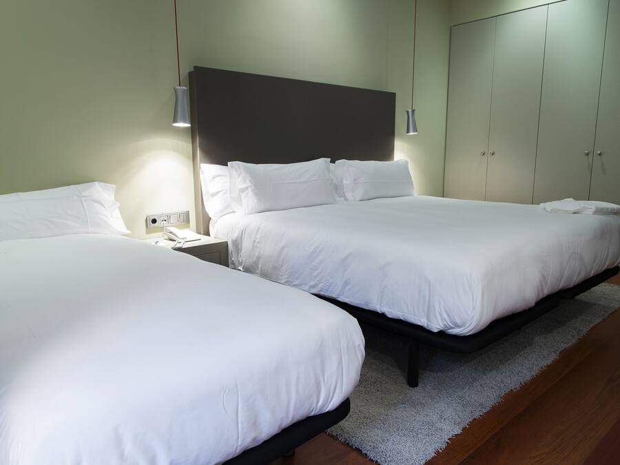 A hotel room with two beds, a large wardrobe, and a bedside table with a lamp.