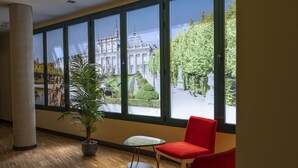 A room with large windows, a potted plant, a small table, and a red chair.