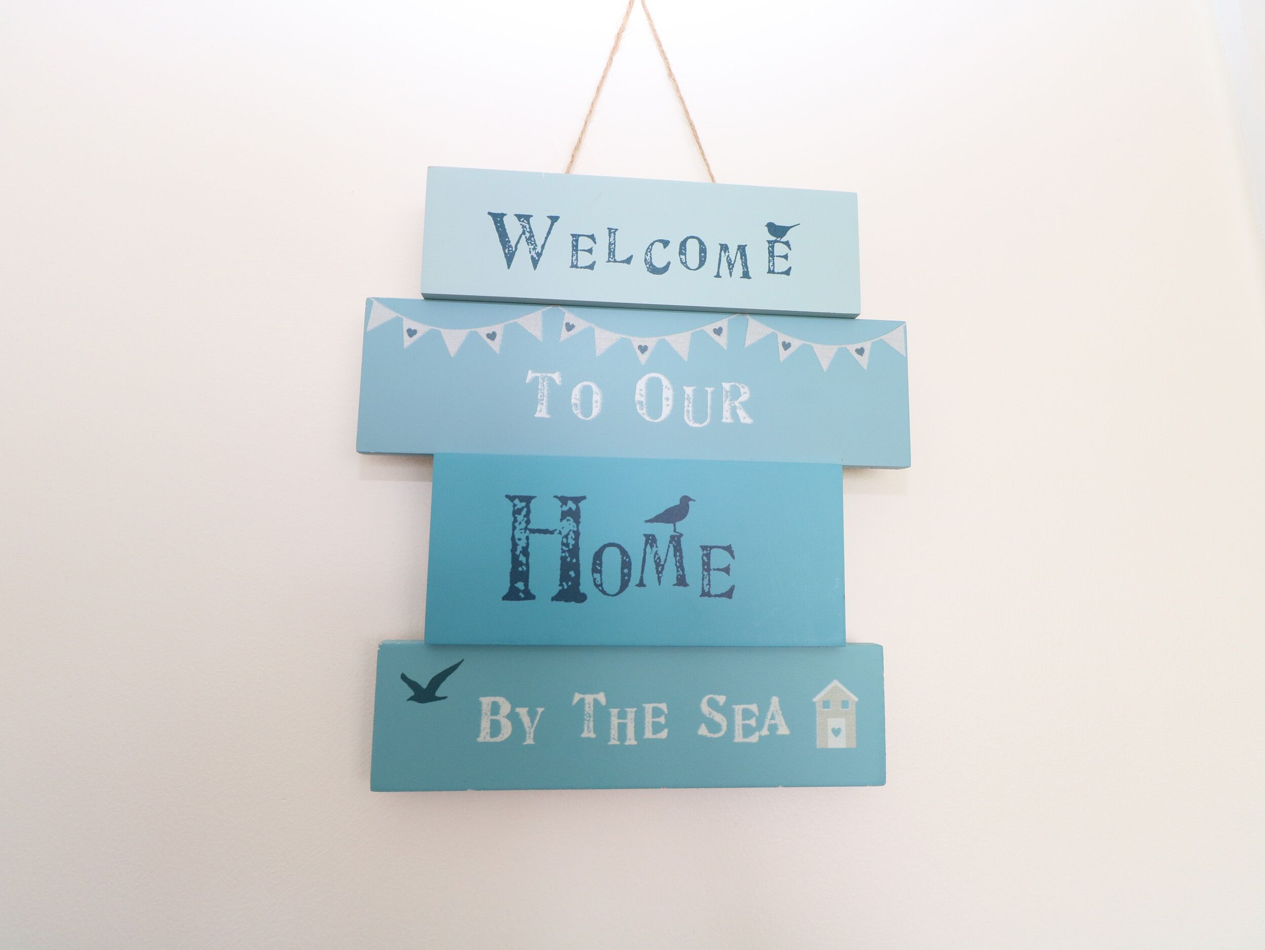 A layered sign with text indicating a welcoming message to a home by the sea.