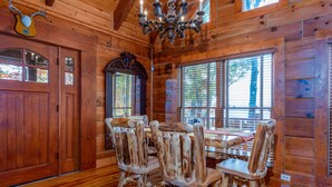 Un interno rustico in legno con zona pranzo, caratterizzato da un lampadario e una testa di cervo appesa al muro.