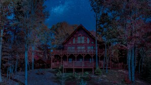 Un'ampia baita di legno con diversi balconi, immersa tra gli alberi e sotto un cielo notturno limpido.