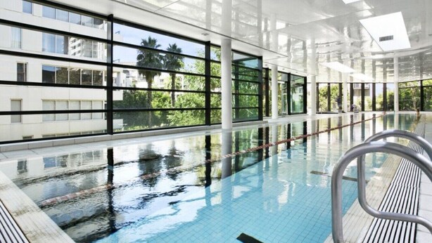 Une piscine intérieure avec des parois en verre transparent, un sol carrelé et des échelles métalliques.