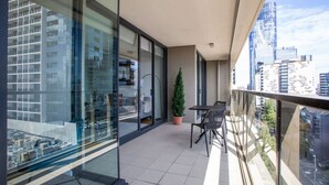 Un balcon moderne avec vue sur la ville, une petite table et des chaises, ainsi qu’une plante en pot.