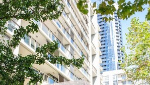 Une entrée d’hôtel moderne, avec un auvent rouge, des portes vitrées et une vue dégagée sur les immeubles environnants.