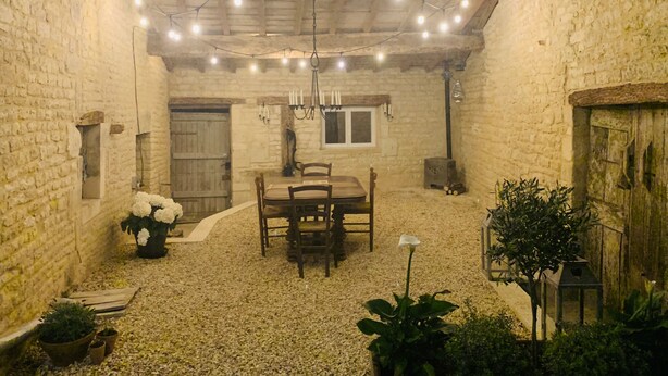 A rustic stone-walled room with a wooden table and chairs, string lights, and potted plants. - Gîte des Ruches, Peaceful & Homely 1 bedroom Gîte with pool (Chives)