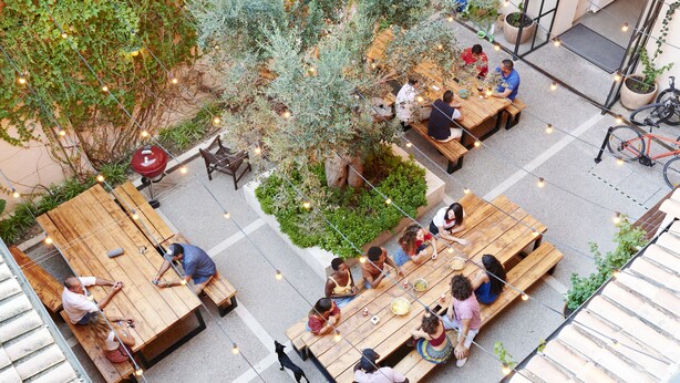An outdoor dining area with wooden tables and benches, surrounded by greenery and string lights. - The Boc Hostels Palma - Youth Hostel (Palma de Mallorca)