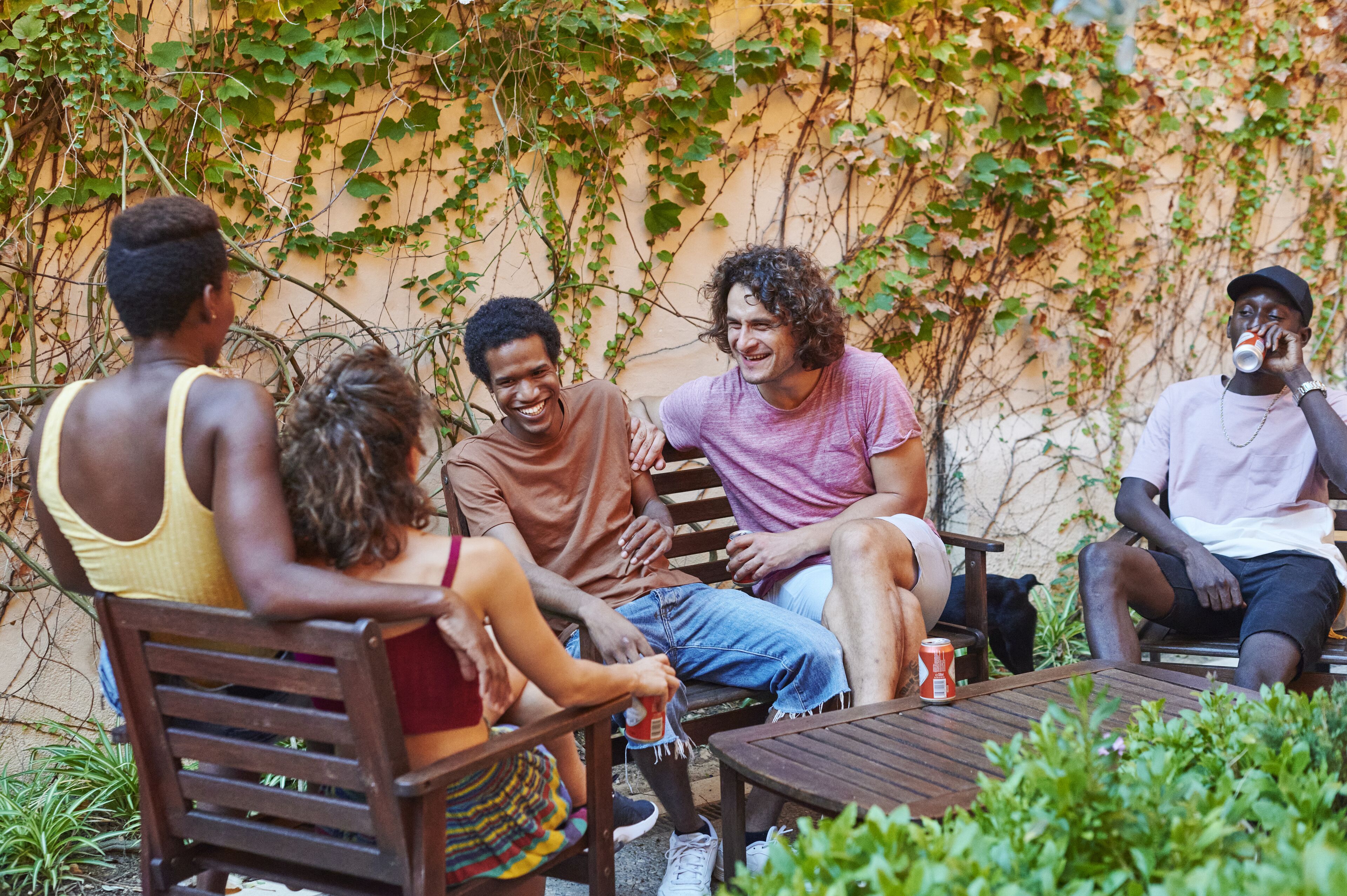 Un grupo de personas sentadas en bancos y sillas de madera al aire libre, conversando.