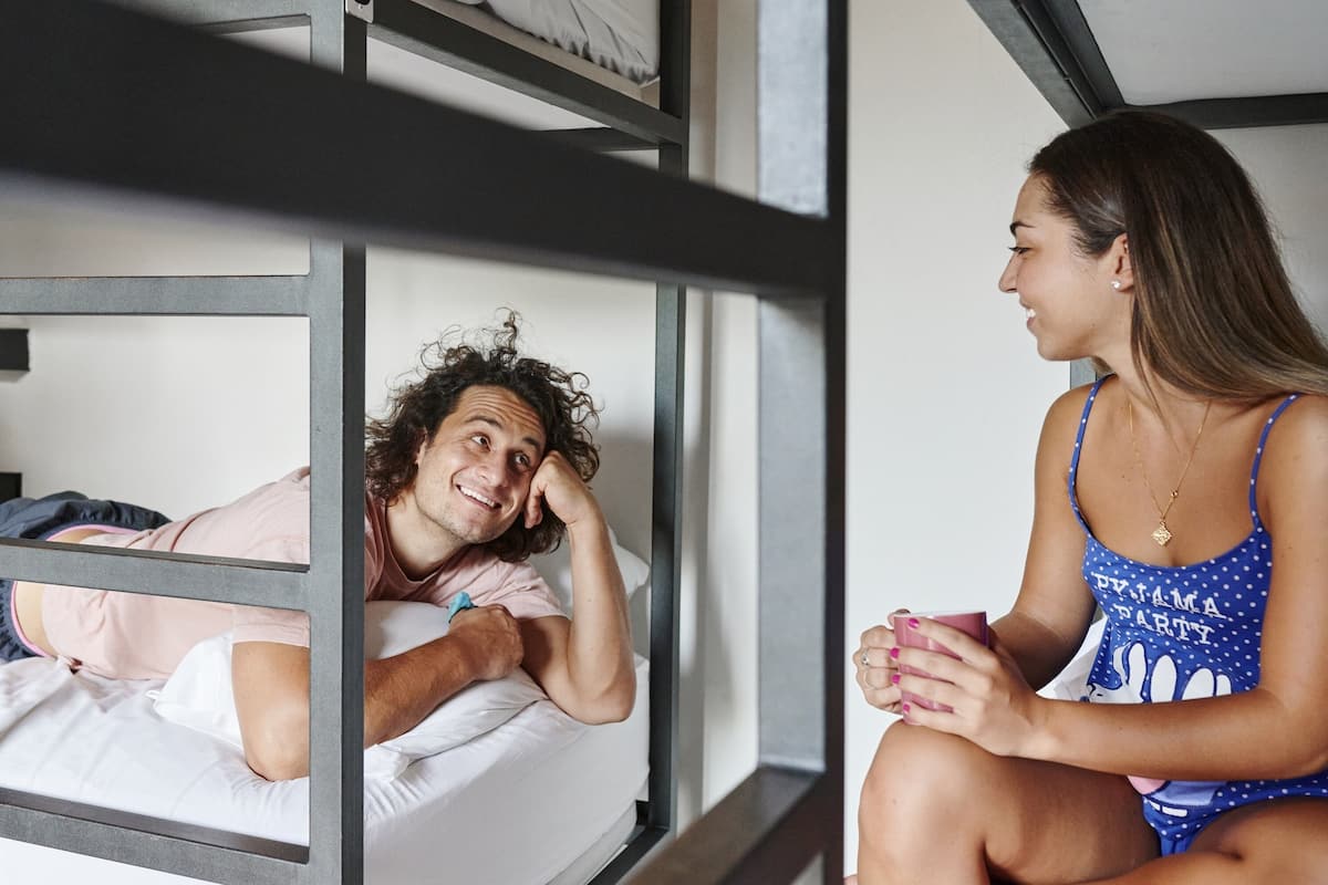 A bunk bed with a person lying on the lower bunk and another person sitting on the floor next to it.