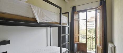 Habitación tipo dormitorio con literas, una ventana con cortinas y un radiador.