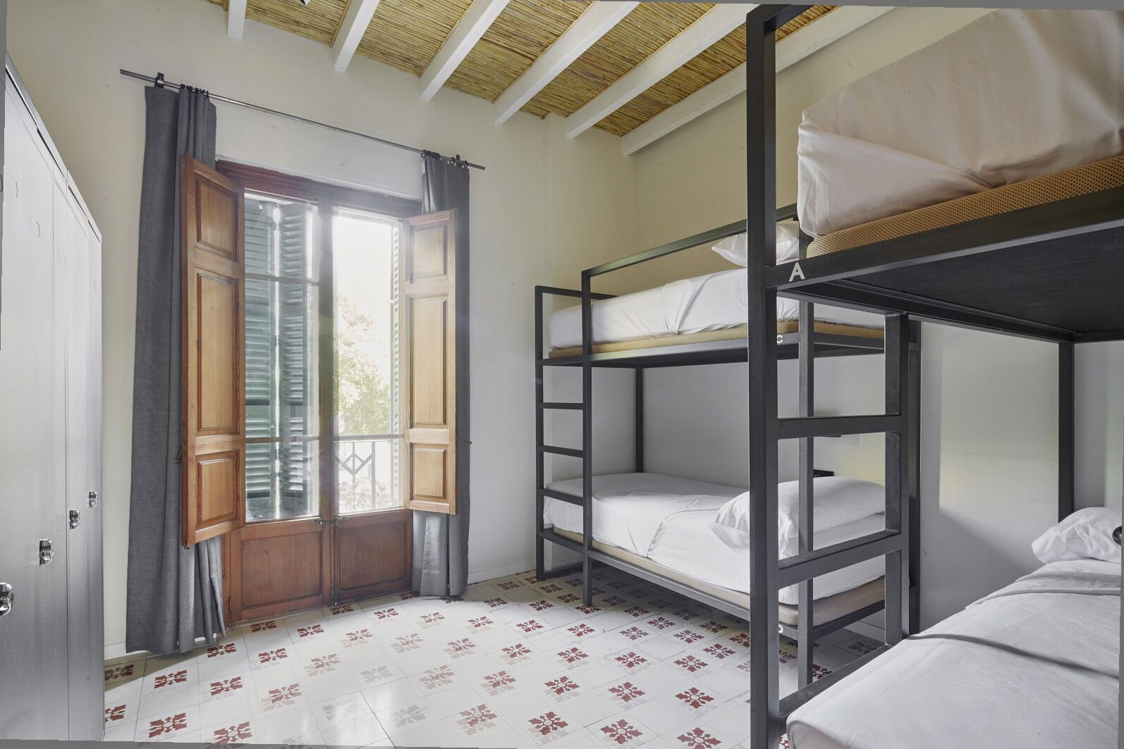 Habitación tipo dormitorio con literas, una ventana con cortinas, un armario y baldosas de suelo estampadas.