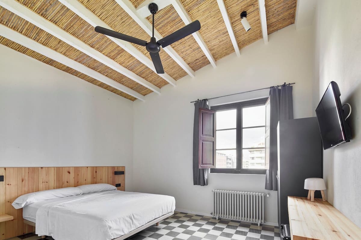 A room with a bed, a desk, a television, and a window with curtains.