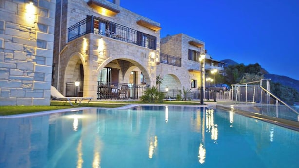 Un edificio de varios pisos de piedra con piscina, mobiliario exterior y vistas del paisaje circundante.