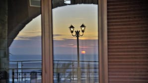 Vista al atardecer a través de una ventana con barandilla de balcón y farola.
