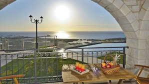 Un balcón con vista al mar, una mesa con una cesta de fruta y un farol.