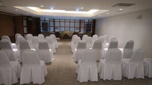 A conference room with rows of white-covered chairs and tables, large windows, and a high ceiling with recessed lighting. - Hotel Fastos (Monterrey)