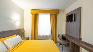 Habitación de hotel con cama, escritorio, silla, televisión y ventana con cortinas.