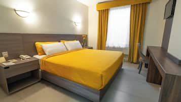 Una habitación de hotel con cama, mesita de noche, lámpara y escritorio con silla.