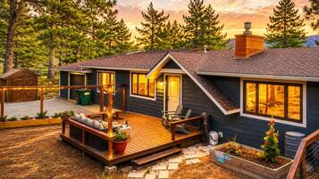 A modern house with a deck, a covered outdoor seating area, and a large window overlooking a forested area.