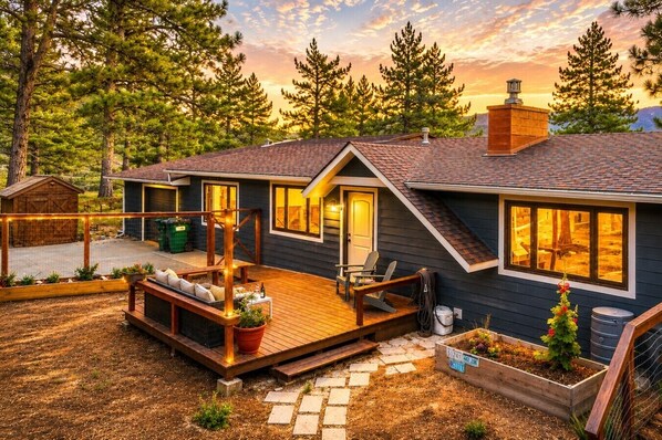 A modern house with a deck, a covered outdoor seating area, and a large window overlooking a forested area.