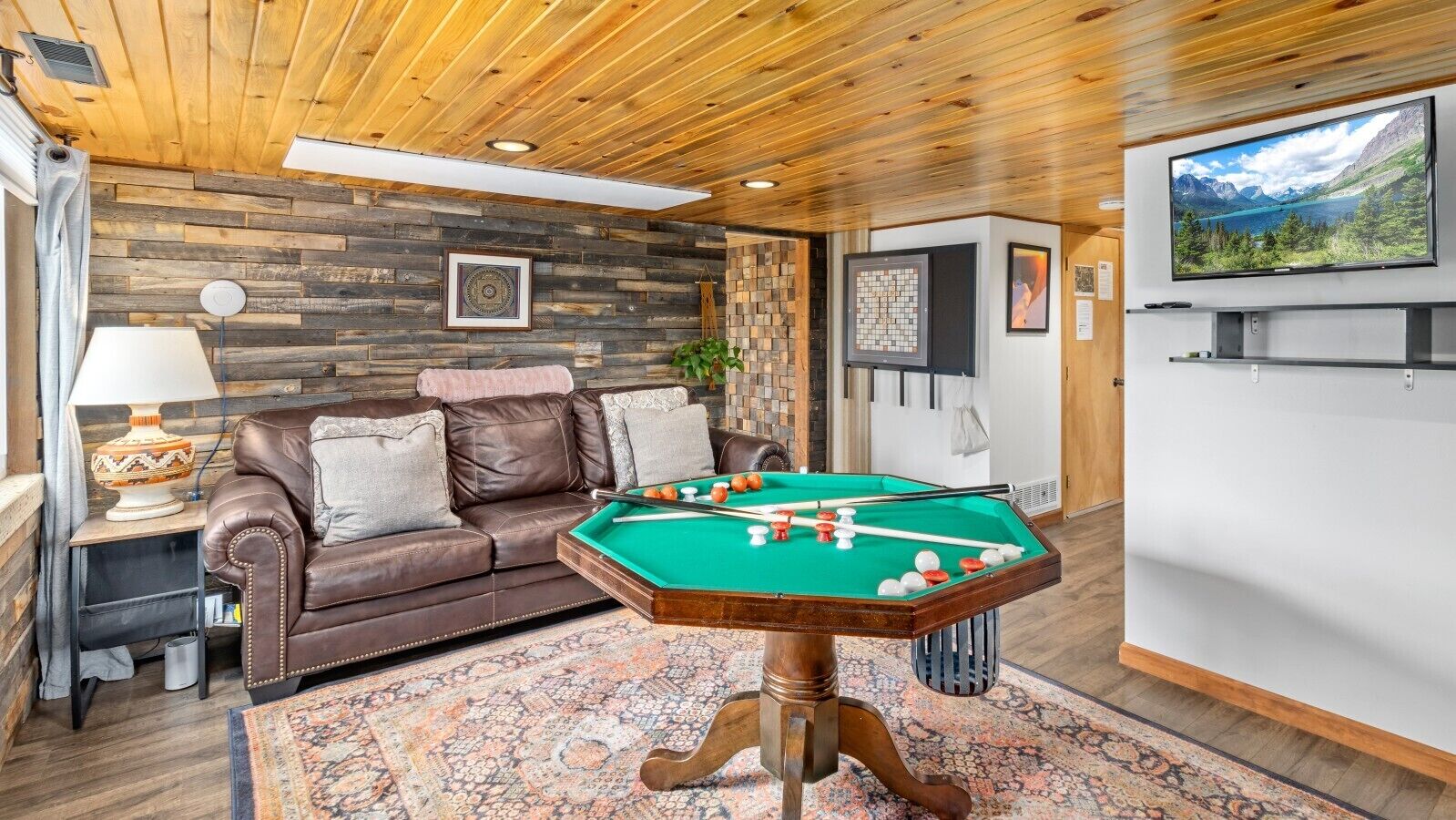 A cozy room with a pool table, a leather sofa, and a television mounted on the wall.