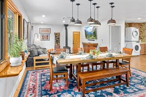 Un coin repas avec une table en bois dressée pour six personnes, entourée de chaises, et un grand tapis sur le sol.