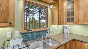 A kitchen with a double sink, wooden cabinets, a window with a view of trees, and a coffee maker on the counter.