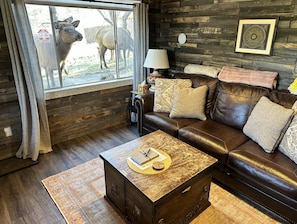 Ein gemütliches Wohnzimmer mit Ledersofa, Holztisch und einem Fenster mit Blick auf eine Kuh.