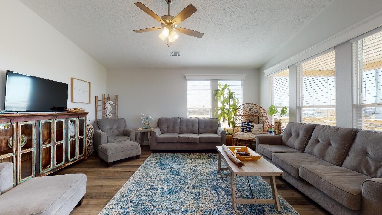 A living room with a ceiling fan, a television, a gray sofa, a coffee table, and a patterned rug.