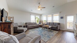 A spacious living room with a ceiling fan, large windows, and a view of the city.