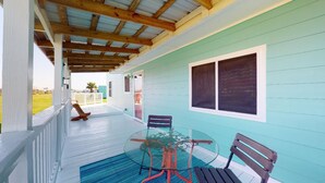 A covered porch with a glass table and chairs, a wooden bench, and a view of a house. - The Mango Hut: 2  BR, 1  BA House in Port Bolivar, Sleeps 8 (Port Bolivar)