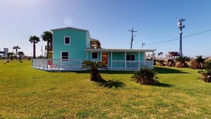 A single-story building with a flat roof, a small porch, and a fenced yard. - The Mango Hut: 2  BR, 1  BA House in Port Bolivar, Sleeps 8 (Port Bolivar)