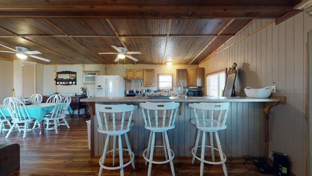 A kitchen with wooden cabinets, a bar area with stools, and a dining area with chairs. - The Mango Hut: 2  BR, 1  BA House in Port Bolivar, Sleeps 8 (Port Bolivar)