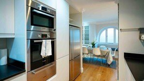 A modern kitchen with stainless steel appliances, a dining area with a table and chairs, and a view of the outdoors through a window. - Spacious & Modern 3brs House in Central London (London)