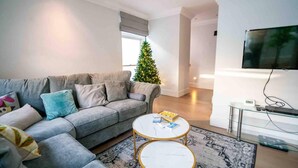 A living room with a grey sofa, two white round tables, a Christmas tree, and a TV on the wall. - Spacious & Modern 3brs House in Central London (London)