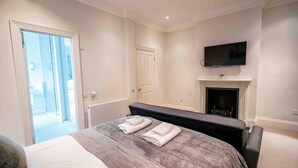 A modern bedroom with a large bed, a fireplace, a TV, and a door leading to a balcony. - Spacious & Modern 3brs House in Central London (London)