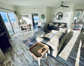 A spacious living room with a large sofa, a coffee table, and a view of the ocean through a sliding glass door.