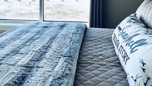 Un dormitorio con una cama grande, vista a la playa y un cartel sobre la ventana que dice 'Cargos por Banco - No se permiten zapatos'.