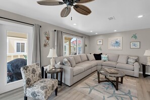A living room with a sectional sofa, a patterned armchair, a coffee table, and a ceiling fan. - 🌊Walk to Beach~Gulf Views~Updated~3BR Regency CabanasE1 (Pensacola Beach)