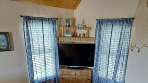 Ein Wohnzimmer mit braunem Ledersofa, passendem Hocker, einer Holzkommode mit Flachbildfernseher und einer kleinen Vitrine mit Dekoration.