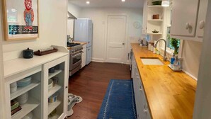 A compact kitchen with white cabinets, a wooden countertop, and a blue rug.