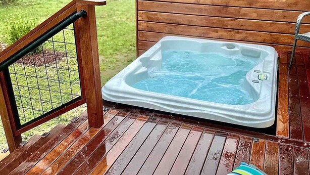A wooden deck with a hot tub, a lounge chair, and a string of lights.
