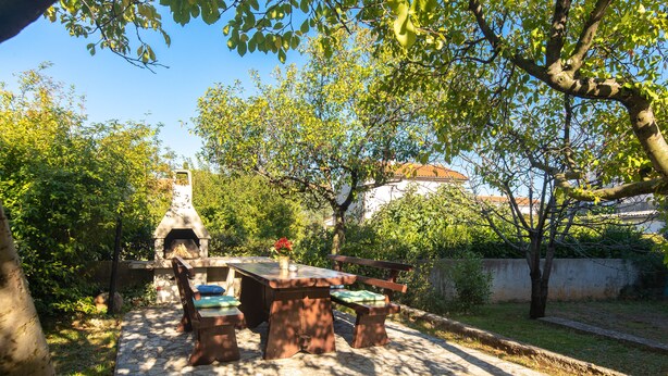 An outdoor patio with a stone table and benches, surrounded by trees and a stone oven. - 2-bedroom Krk Apartment - Near Krk Beaches & Town! (Krk)