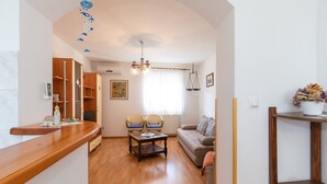 A living room with a wooden coffee table, two chairs, a sofa, a wooden shelf, and a window with curtains. - 2-bedroom Krk Apartment - Near Krk Beaches & Town! (Krk)