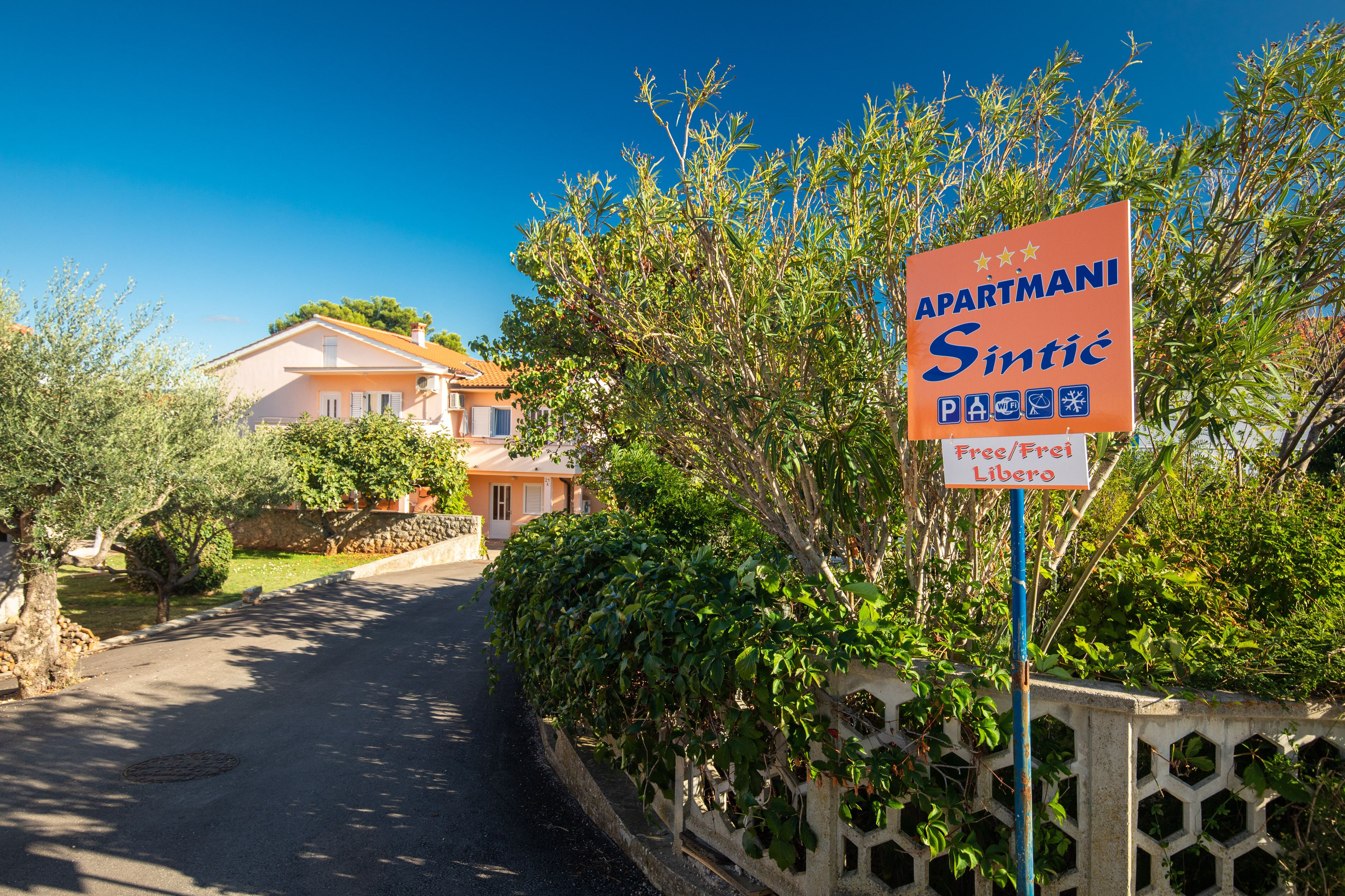 Une enseigne indiquant un établissement appelé « APARTMANI Sintic », qui propose des équipements tels qu’un parking gratuit et une piscine.