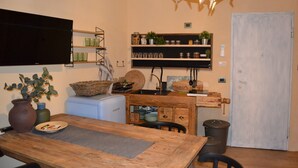 Eine Küche mit einem Holztisch, einem Fernseher, Regalen mit Gläsern und Pflanzen sowie einer Tür.