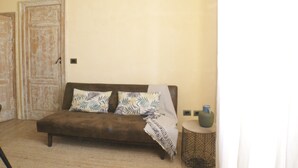 Ein Zimmer mit einem braunen Sofa, zwei gemusterten Kissen, einer gestreiften Decke, einem kleinen runden Tisch mit einer Vase und einer Tür im Hintergrund.