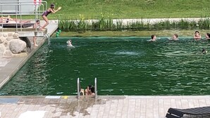 Une piscine avec un plongeoir, un poste de surveillance pour les sauveteurs et des personnes qui nagent.